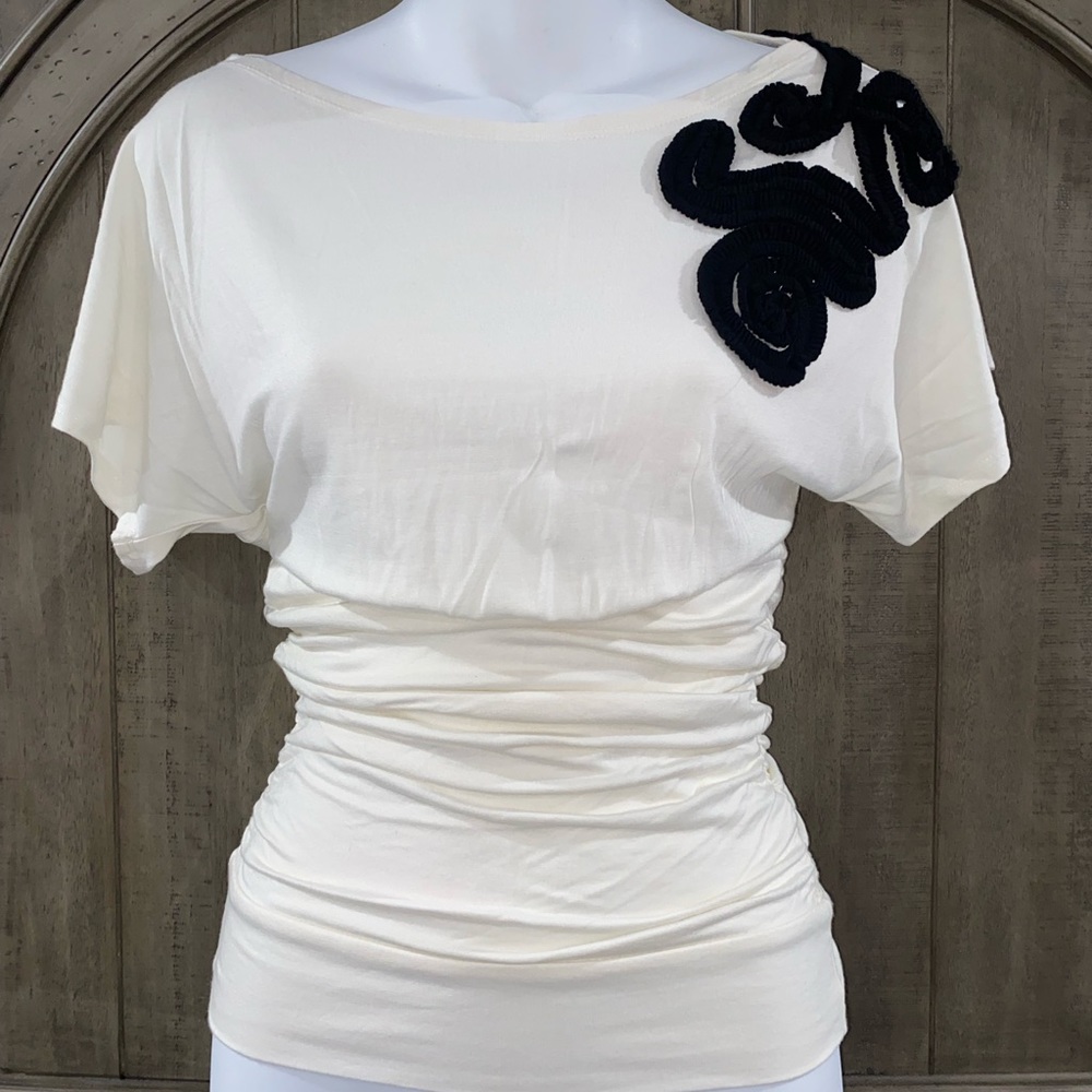 Cream colored top with a black decorative piece on it